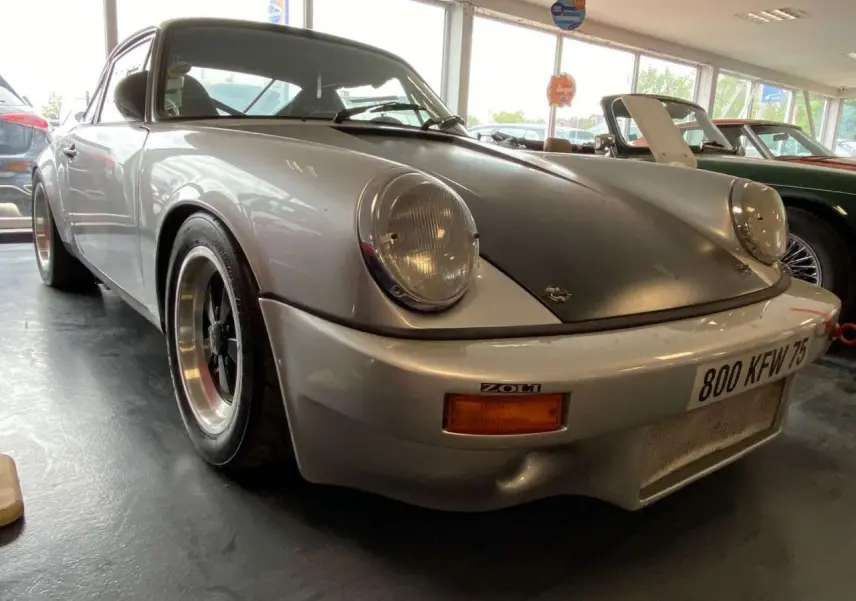 Porsche 911 3.0 SC gris métallisé vue 3/4 avant avec capot noir mat et jantes alliage Fuchs.