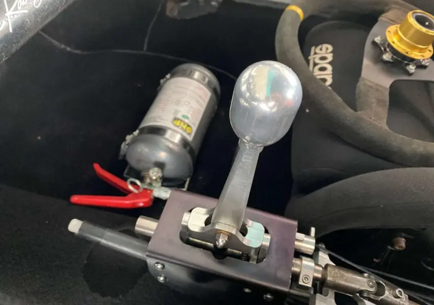 Gros plan sur le levier de vitesses manuel rigide et siège baquet Sparco noir dans l’habitacle d’une Porsche 911 gris métallisé.