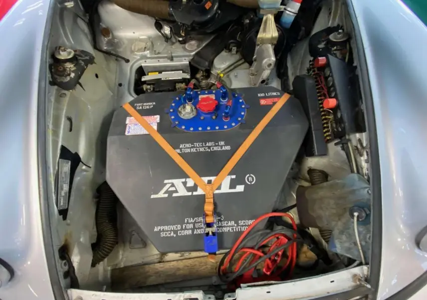 Vue plongeante sur le compartiment avant gris métallisé d’une Porsche 911 3.0 SC avec réservoir FIA et sangles orange.