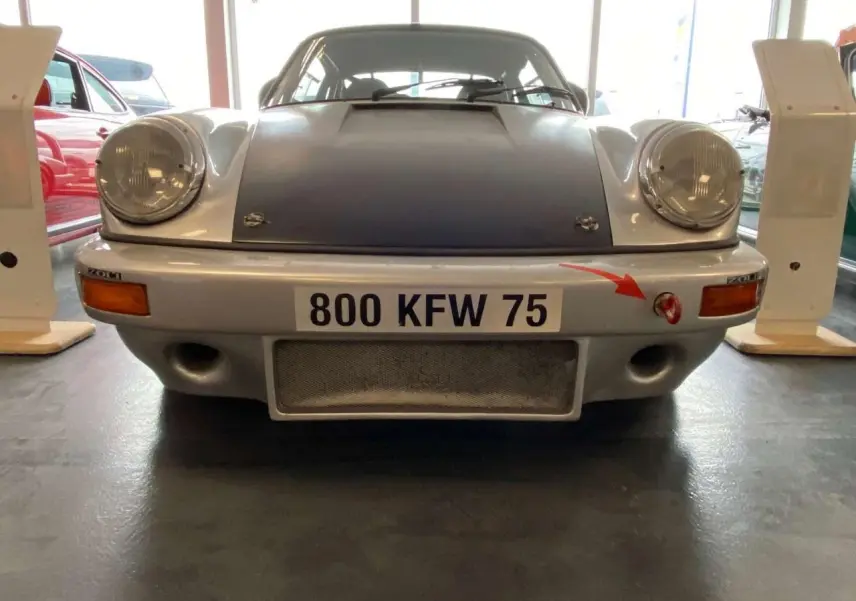 Vue frontale d'une Porsche 911 3.0 SC gris métallisé avec capot noir mat et attache rouge sur pare-chocs.
