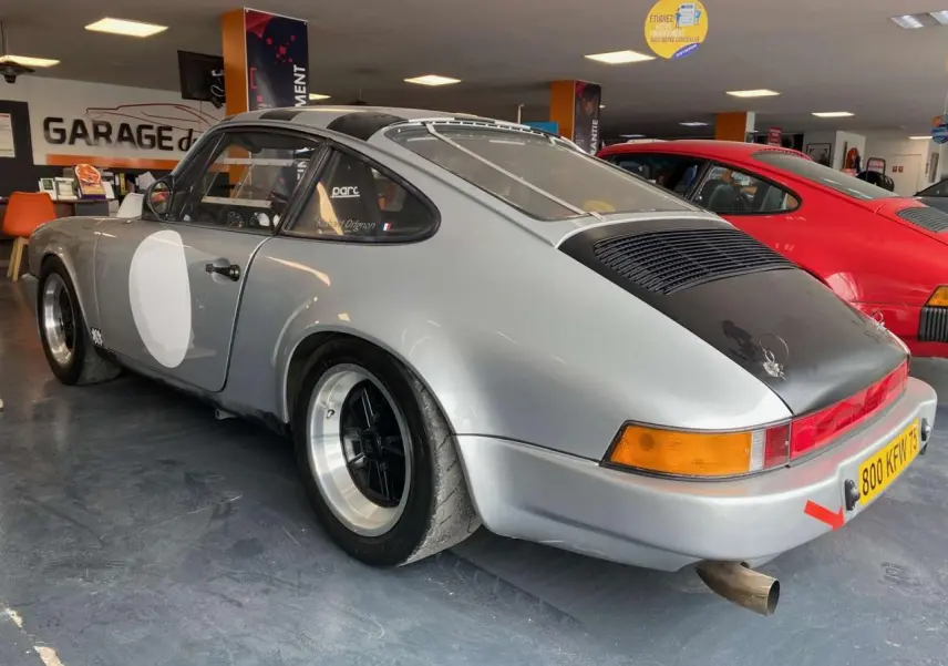 Vue 3/4 arrière droite d'une Porsche 911 3.0 SC 930 gris métallisé avec jantes Fuchs et vitre arrière Lexan en intérieur de garage.