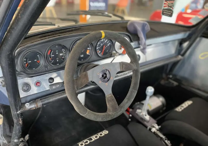 Vue intérieure côté conducteur du tableau de bord aluminium et volant Sparco d’une Porsche 911 3.0 SC course.