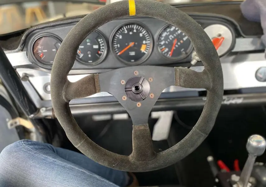 Vue intérieure centrée sur le volant Sparco en alcantara et le tableau de bord de la Porsche 911 3.0 SC gris métallisé.