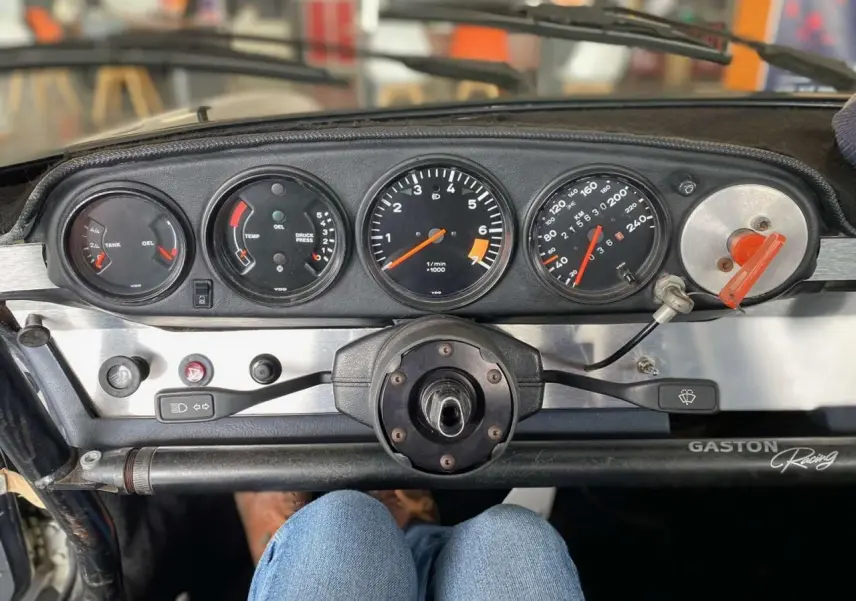 Tableau de bord de Porsche 911 3.0 SC gris, vue frontale centrée sur les compteurs et volant Sparco sans moyeu.