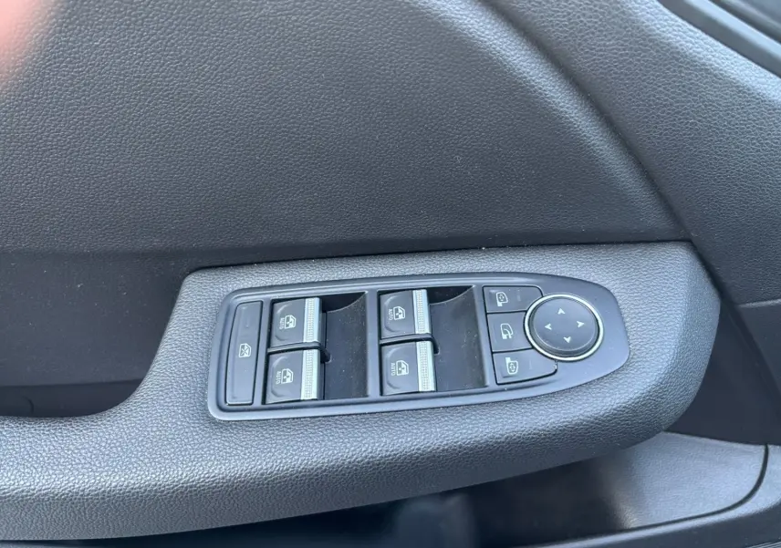 Gros plan sur les commandes des vitres électriques et des rétroviseurs sur la porte côté conducteur d'une Renault Clio gris foncé.