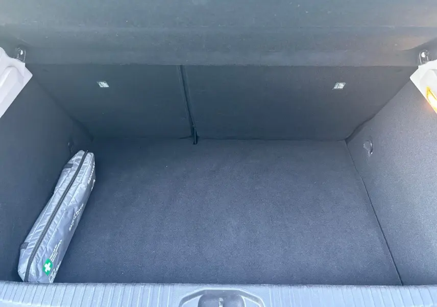 Coffre ouvert de la Renault Clio 1.6 E-TECH Business gris foncé, montrant un espace vide avec trousse de secours à gauche.