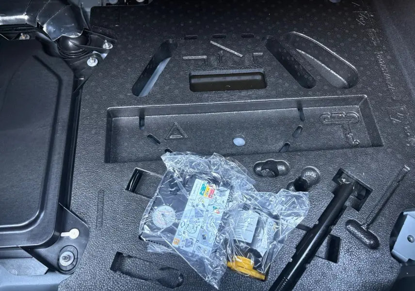 Gros plan sur le kit anti-crevaison dans le coffre d’une Renault Clio 1.6 E-TECH gris foncé, année 2021.