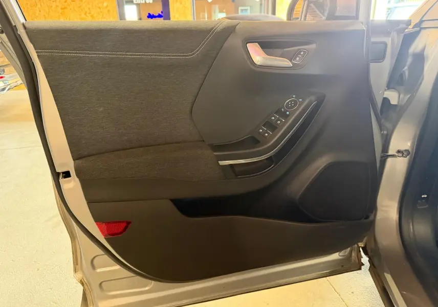 Vue intérieure de la porte avant gauche grise du Ford Puma 1.0 EcoBoost 125 MHEV Titanium avec commandes électriques.