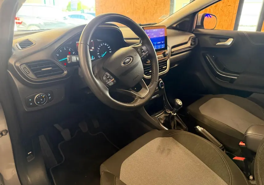 Vue intérieure côté conducteur du Ford Puma gris 2021, volant multifonction, tableau de bord digital et levier de vitesse manuel.