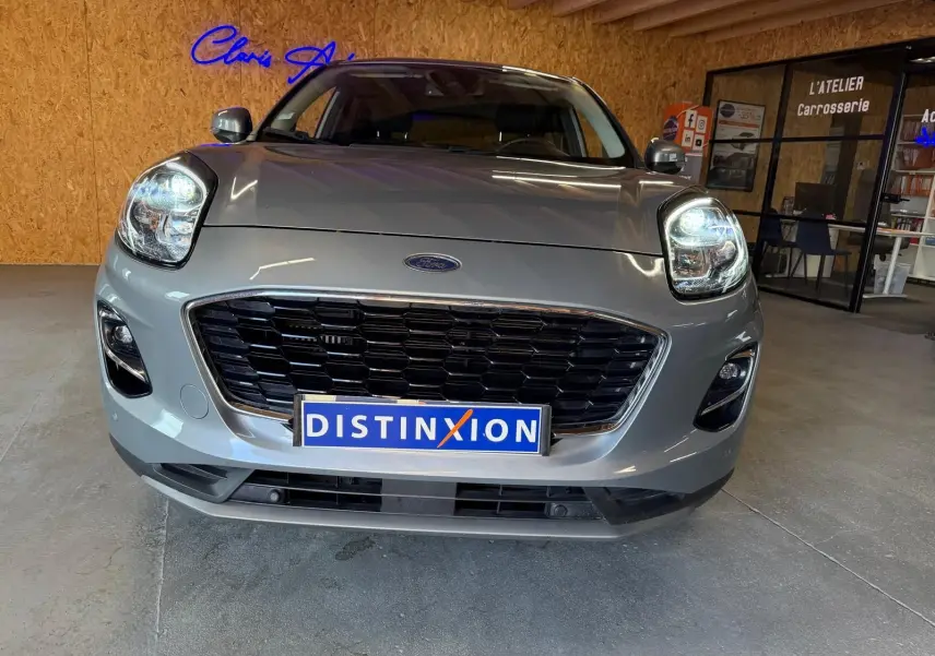 Vue avant rapprochée du Ford Puma gris 2021 avec calandre noire et phares allumés en intérieur showroom.