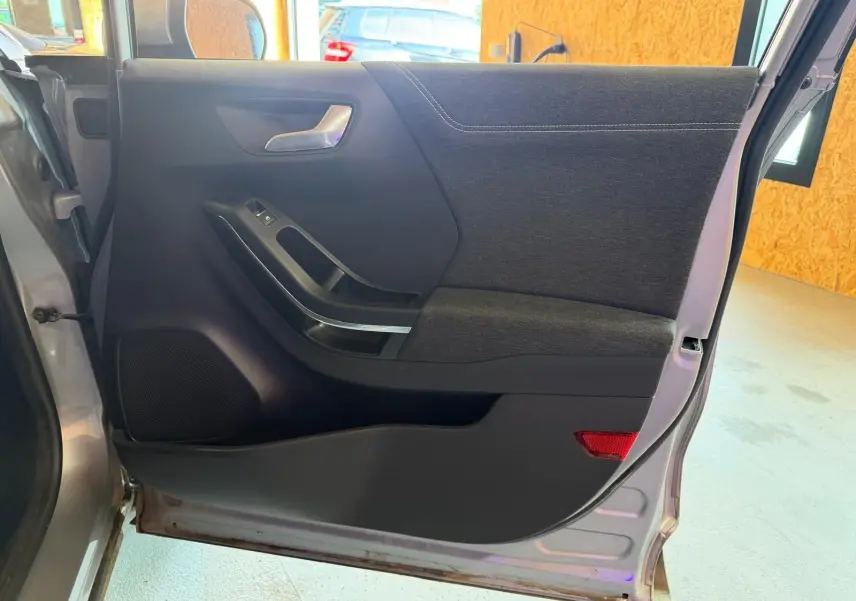 Vue intérieure côté gauche de la porte arrière grise du Ford Puma 2021 avec garniture tissu noir et poignée argentée.