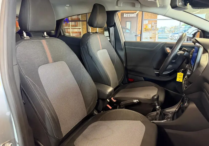 Vue intérieure côté conducteur du Ford Puma gris 2021, sièges tissu noir avec console centrale et levier de vitesses manuel.