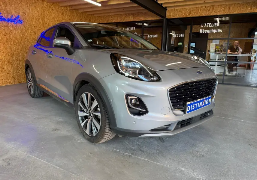 Ford Puma gris vue 3/4 avant droit dans un garage avec calandre noire et jantes alliage distinctives.