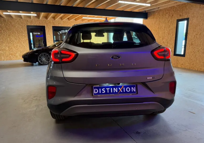 Vue arrière d'une Ford Puma gris métallisé 2021, avec feux arrière allumés et plaque Distinxion visible.