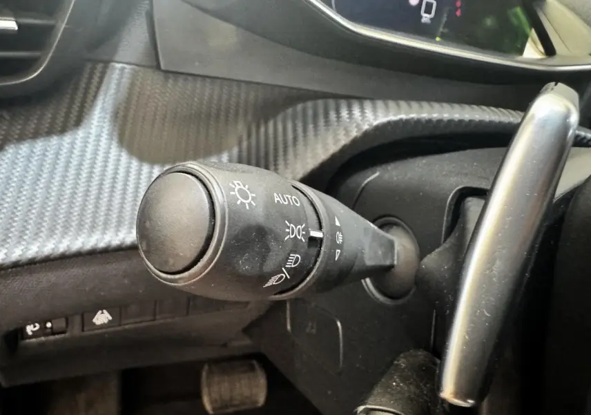 Gros plan sur la commande des phares à gauche du volant dans l’habitacle noir du Peugeot 2008 2022.