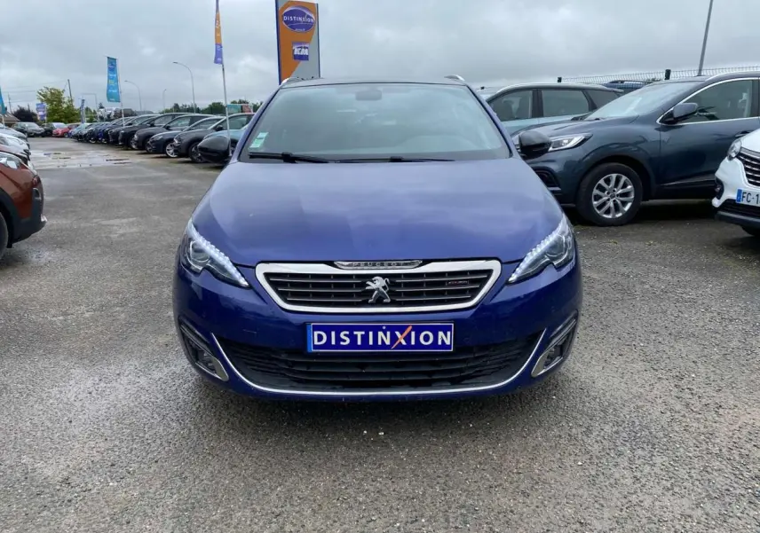 Vue frontale d'une Peugeot 308 SW GT Line bleu magnétique, avec calandre chromée et feux LED allumés.