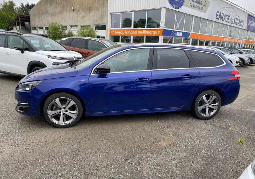 Peugeot 308 SW bleu magnétique vue de profil côté gauche sur parking devant garage multimarque.