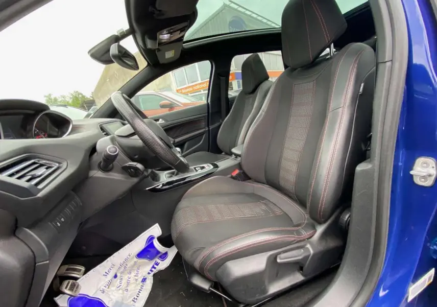 Vue intérieure côté conducteur de la Peugeot 308 SW bleu magnétique, sièges TEP/tissu noirs avec surpiqûres rouges et toit panoramique.