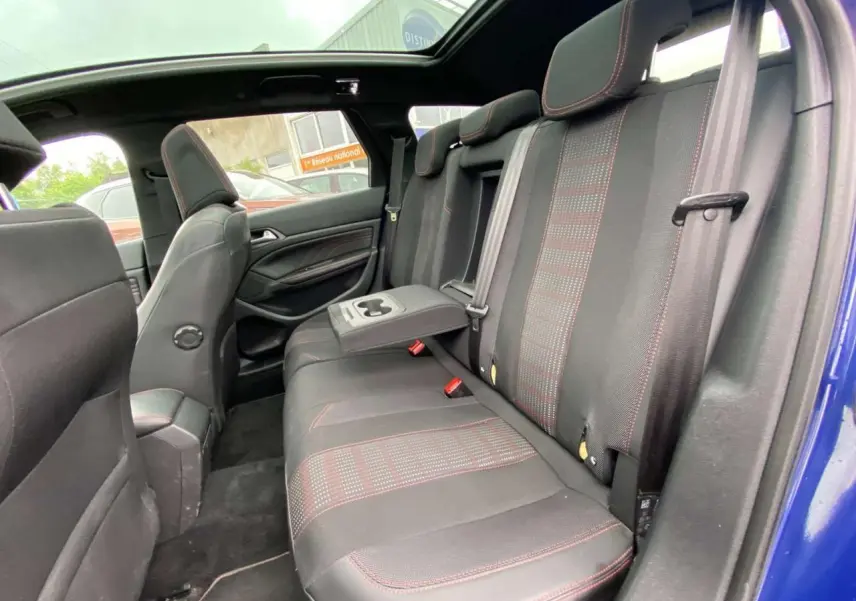 Vue intérieure côté droit des sièges arrière d'une Peugeot 308 SW bleu magnétique avec surpiqûres rouges et toit panoramique.