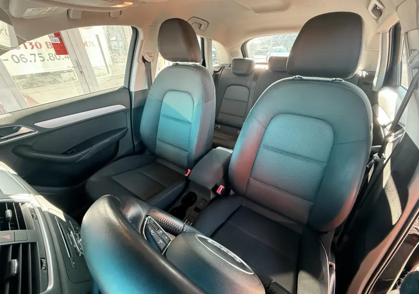 Vue intérieure avant de l'Audi Q3 2016, sièges tissu noirs, volant partiellement visible, ambiance lumineuse naturelle.