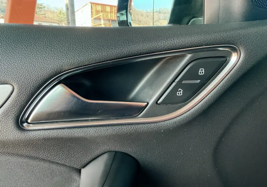 Poignée intérieure côté gauche avec boutons de verrouillage sur la porte d'un Audi Q3 noir, vue rapprochée.