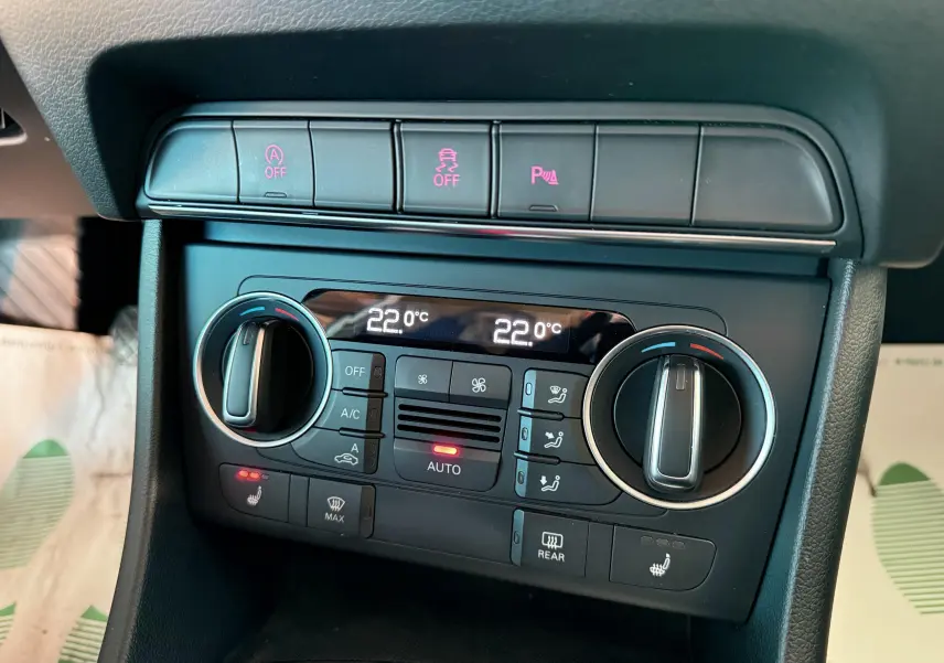 Gros plan sur la console centrale de l'Audi Q3 2016 noire, montrant les commandes de climatisation digitale et les boutons d'assistance.