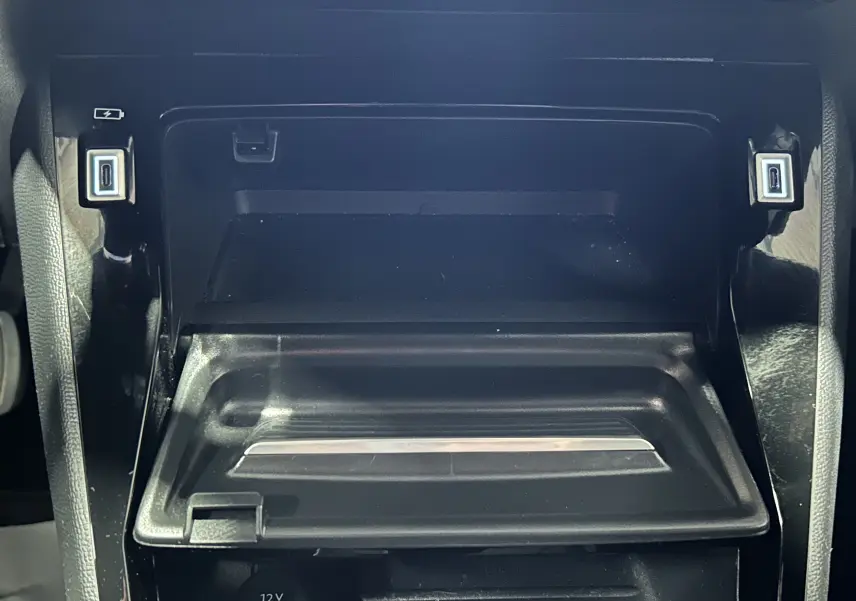 Gros plan sur la console centrale noire du Peugeot 2008 II Ph.2 Allure Hybrid, avec compartiment ouvert et prises USB visibles.