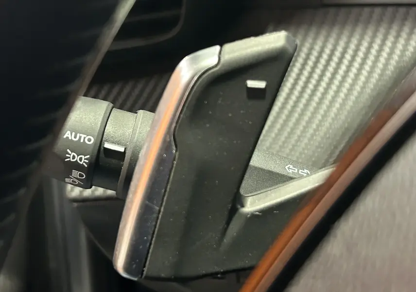 Gros plan sur la commande de clignotant et éclairage, avec palettes de changement de vitesse en aluminium brossé.