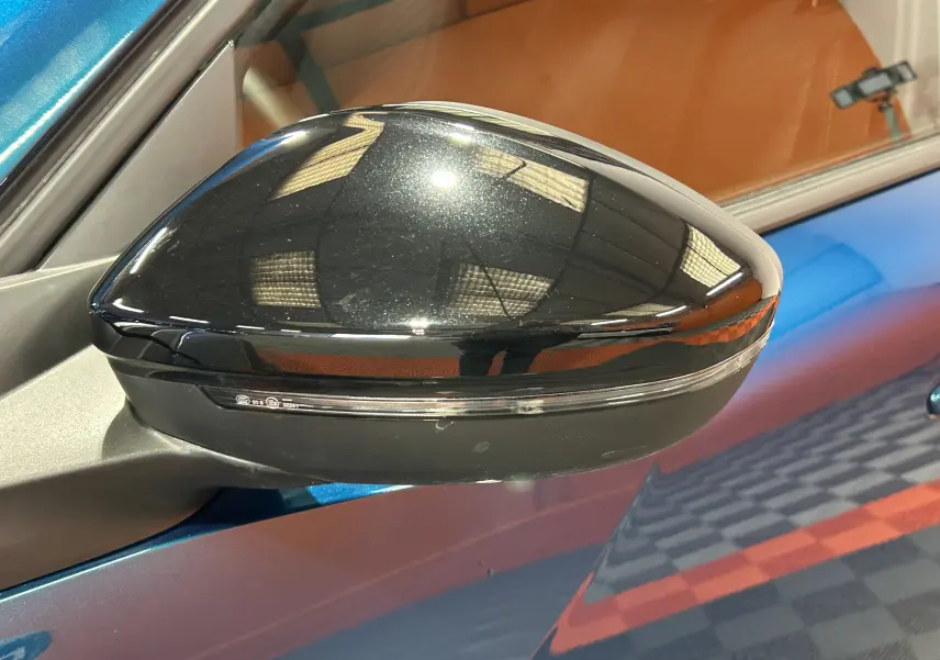 Rétroviseur droit noir brillant sur Peugeot 2008 Bleu Obsession, reflet de l'éclairage intérieur visible.