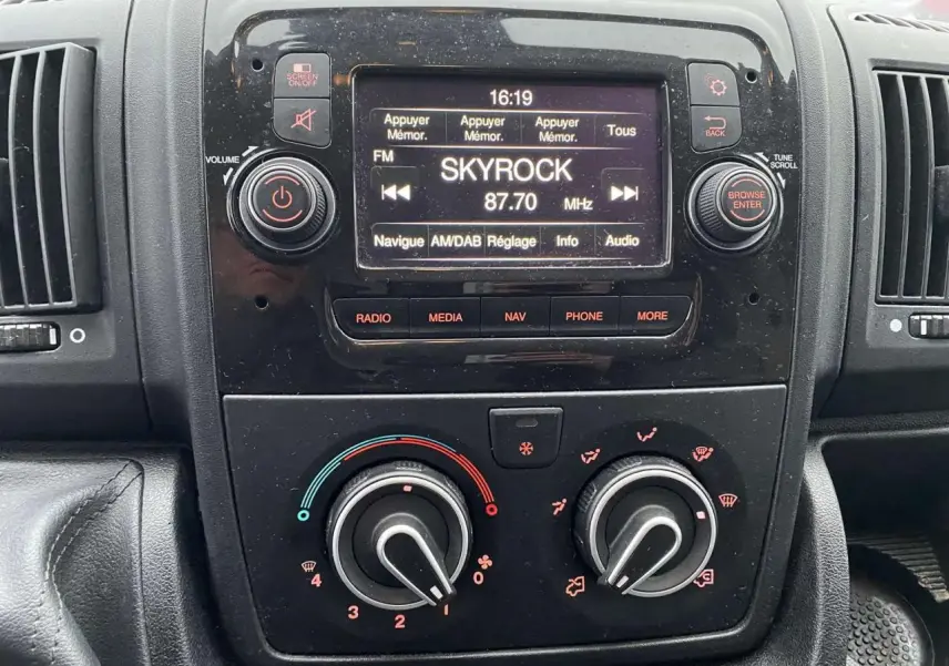 Vue rapprochée du tableau de bord noir de l'Opel Movano Fourgon blanc, avec écran radio affichant Skyrock 87.7 MHz.