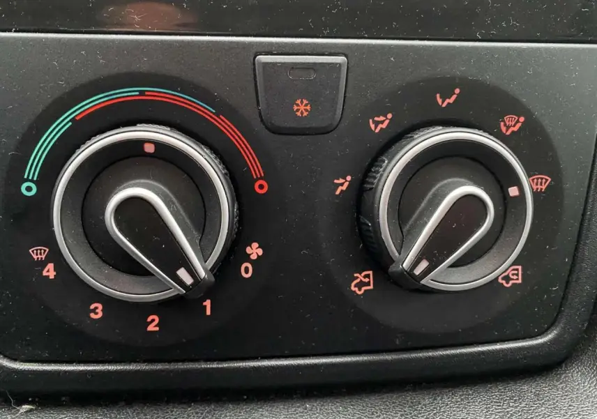 Gros plan sur les commandes de climatisation noires de l’Opel Movano Fourgon blanc, détails des réglages en rouge et bleu.