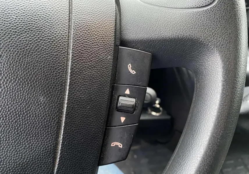 Gros plan sur les commandes de téléphone intégrées au volant noir d’un Opel Movano Fourgon blanc.