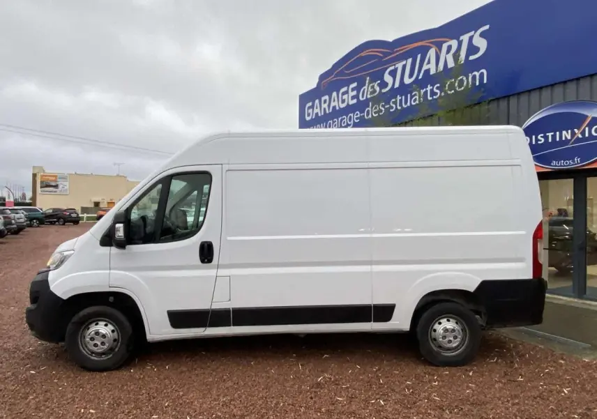 Vue de profil côté gauche d'un fourgon blanc Opel Movano 3.5T L2H2 stationné devant un garage.