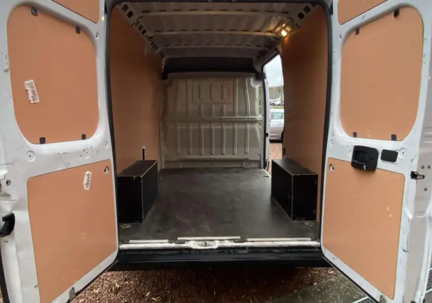 Vue arrière ouverte du fourgon blanc Opel Movano 2022, montrant l'intérieur avec plancher bois et panneaux latéraux beiges.