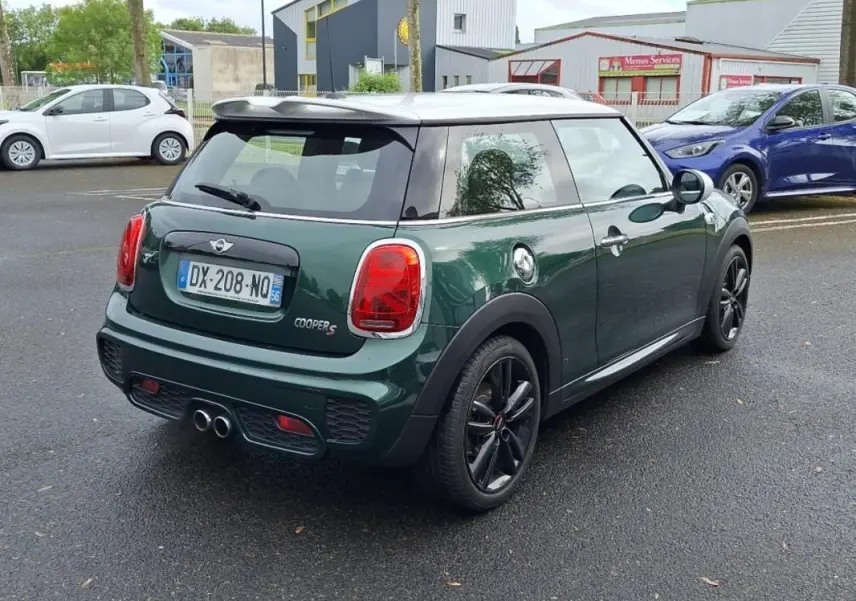 Vue 3/4 arrière d'une MINI Cooper S finition John Work verte avec toit blanc et jantes noires sur parking extérieur.