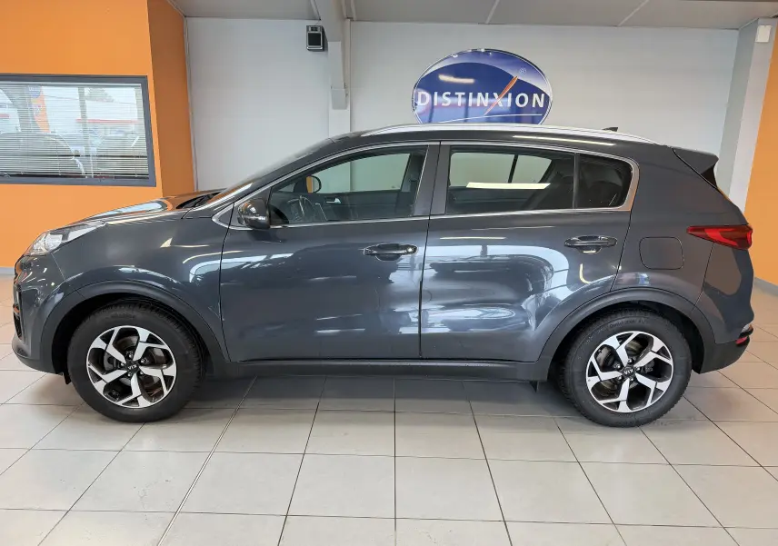 Vue de profil côté gauche d'un KIA Sportage gris 2019 en version 1.6 CRDI 136 Active 4x2, stationné en intérieur.