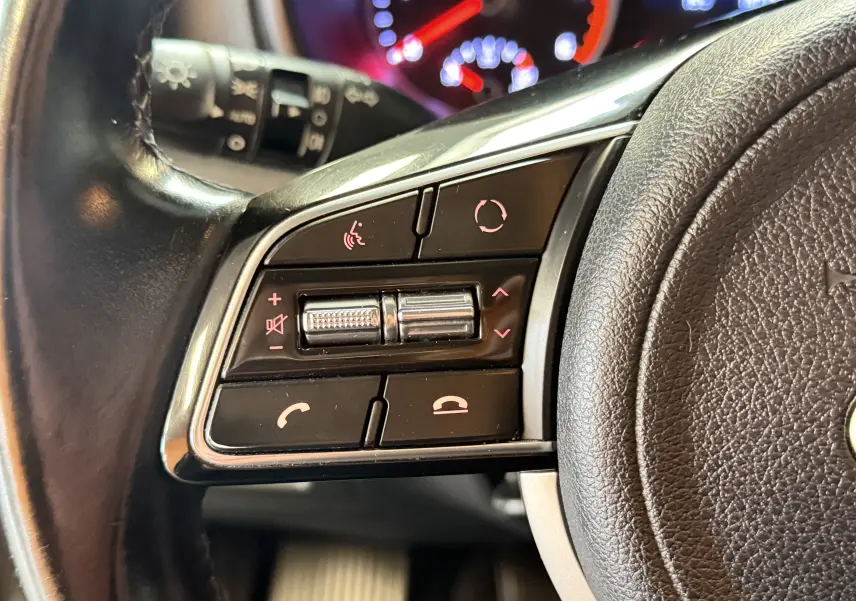 Gros plan sur les commandes au volant côté gauche du Kia Sportage gris 2019, avec boutons multifonctions rétroéclairés rouges.