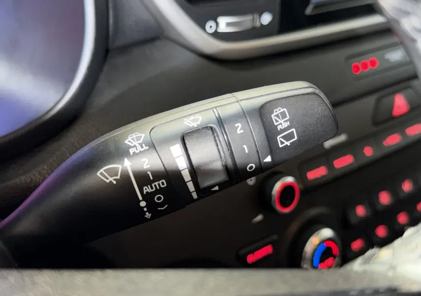 Gros plan sur la commande des essuie-glaces du tableau de bord d’un KIA Sportage gris 2019, avec éclairage rouge.