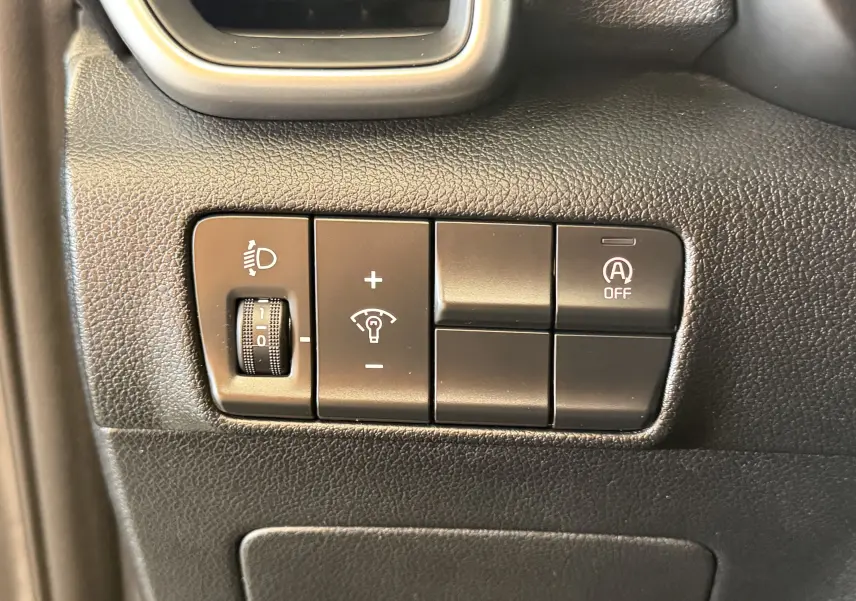 Gros plan sur les commandes intérieures du tableau de bord du Kia Sportage gris 2019, réglage des phares et arrêt du système start-stop.