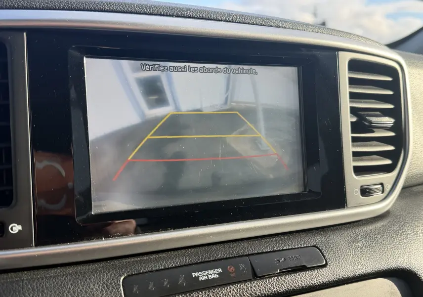 Écran de caméra de recul affichant les lignes de guidage dans un KIA Sportage gris, vue intérieure du tableau de bord.