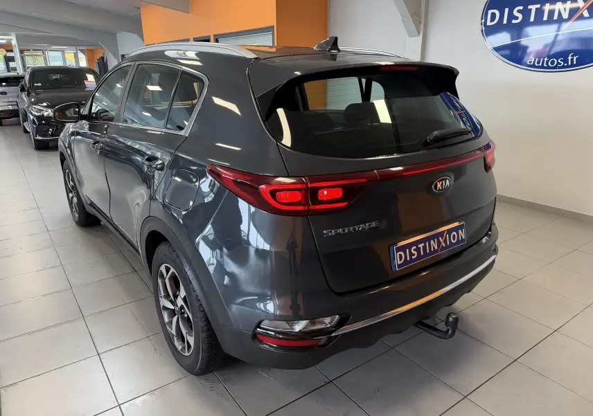Vue 3/4 arrière droite d'un KIA Sportage gris 2019 avec attelage, stationné en intérieur showroom.