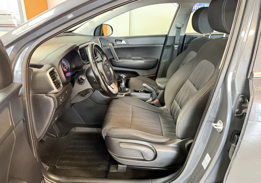 Vue intérieure côté conducteur d'un Kia Sportage gris 2019, montrant les sièges avant et le tableau de bord.