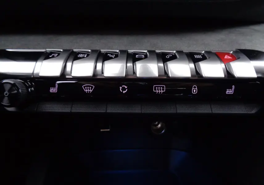 Gros plan sur la rangée de boutons argentés et noirs du tableau de bord du Peugeot 5008 gris platinium, avec commandes éclairées.