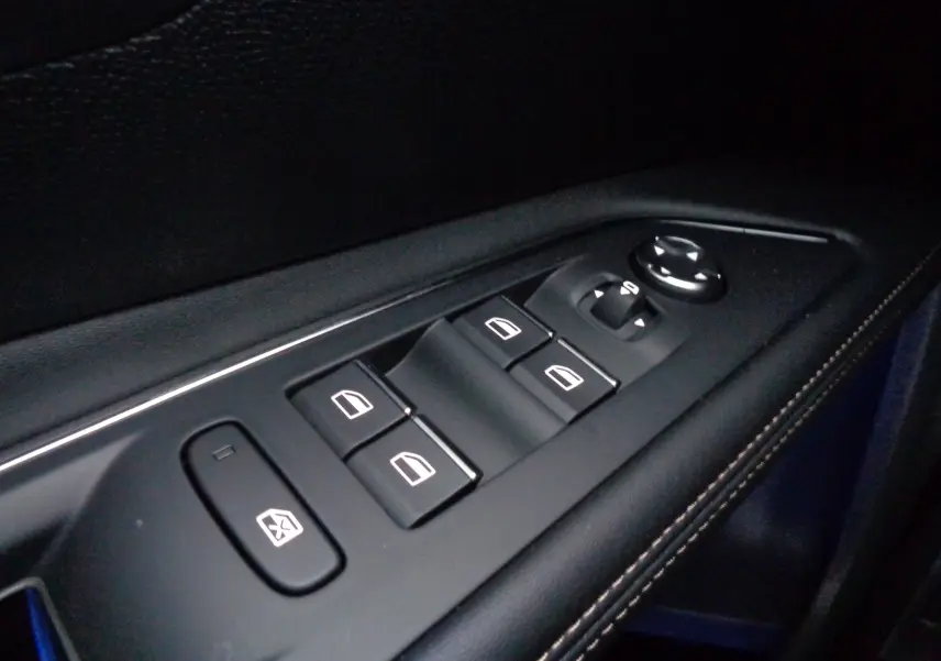 Gros plan sur les commandes des vitres électriques et des rétroviseurs sur la porte intérieure d'un Peugeot 5008 gris platinium 2023.