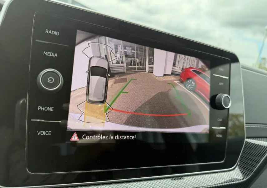 Écran de caméra de recul du Volkswagen T-Cross gris cendre montrant une vue arrière avec lignes de guidage colorées.