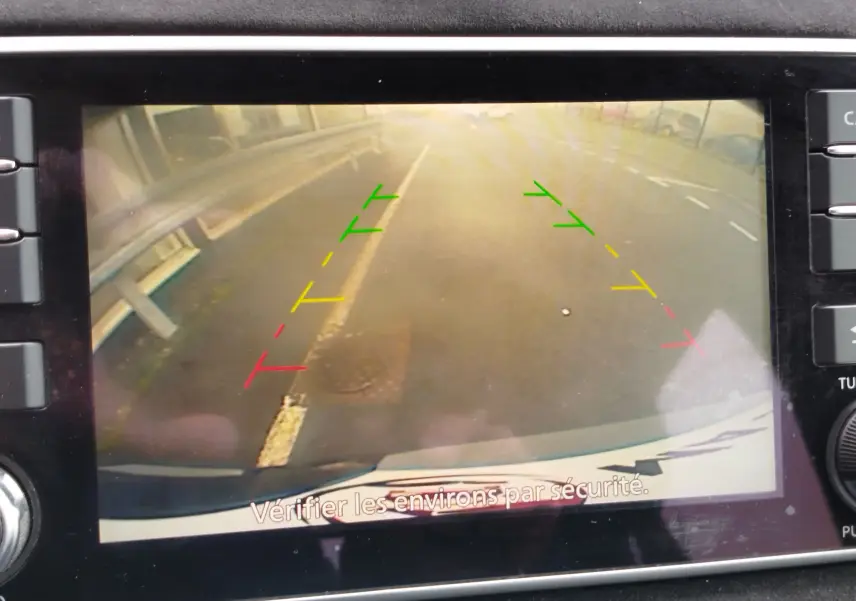 Image de la caméra de recul d'une Nissan Micra noire, affichant les lignes de guidage colorées sur la route arrière.