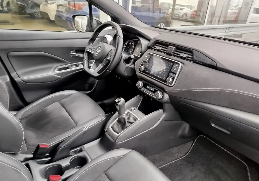 Intérieur noir de la Nissan Micra 2022, vue côté conducteur, avec tableau de bord moderne et levier de vitesse manuel.