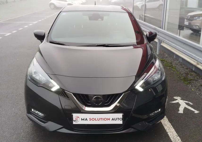 Vue frontale d'une Nissan Micra 1.0 IG-T 92ch N-Sport noire avec phares LED allumés sur parking extérieur.