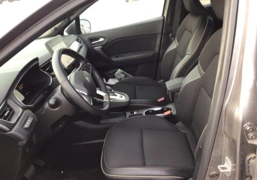 Vue intérieure côté conducteur de la Renault SYMBIOZ gris Cassiopée, sièges noirs avec surpiqûres claires et console centrale moderne.