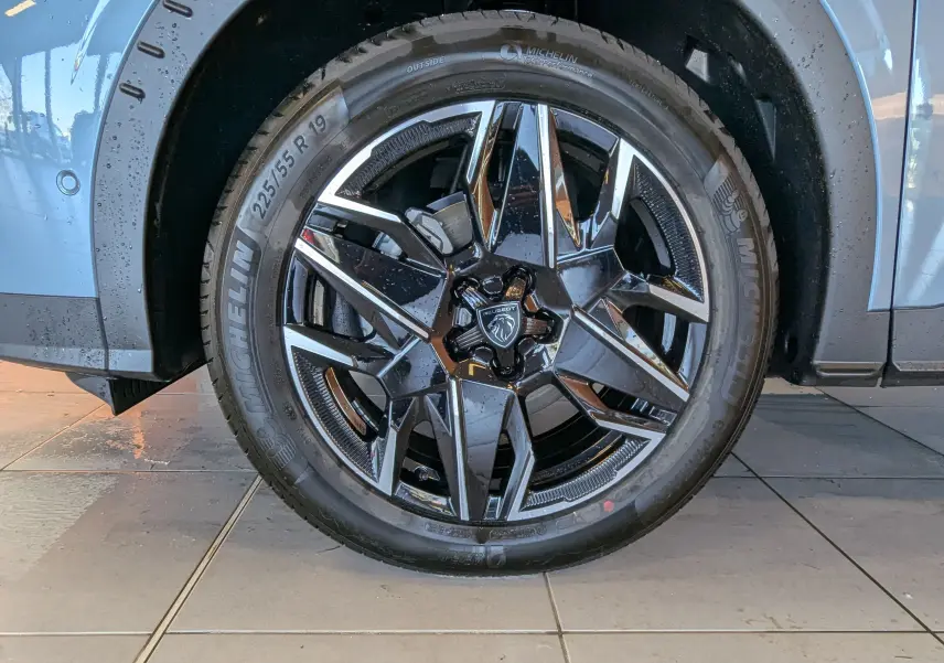 Gros plan sur la roue avant droite bleu Ingaro du Peugeot 3008 1.2 Hybrid avec jante alliage noire et argentée.